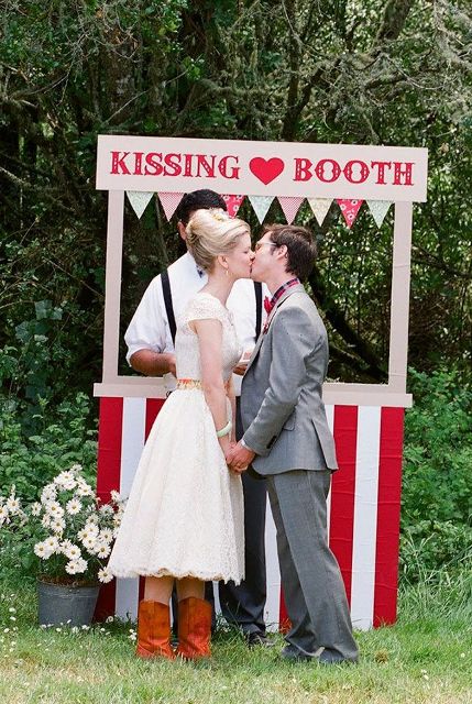 a bright striped kissing booth with a colorful bunting and potted blooms next to it