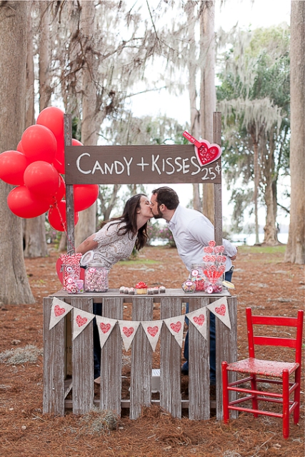 a kissing booth dessert table made of pallets, a sign on top, a heart banner and bright red balloons