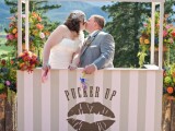 a neutral striped kissing booth decorated with bright blooms and with the same flowers as a backdrop for fun