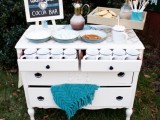 a simple and nice hot cocoa bar of a white sideboard, with a blanket, a sign, a tray with cookies and a carafe