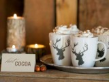 a small hot cocoa bar with a tray with deer mugs, a card and some candles in branch candleholders