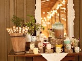 a rustic vintage hot cocoa bar done with a vintage table, tree stumps, greenery in a jug and a vintage mirror and doily
