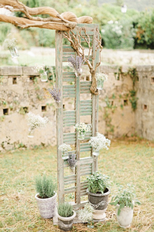 A shutter decorated with branches, floral arrangements and various potted plants is a cool idea for many types of weddings