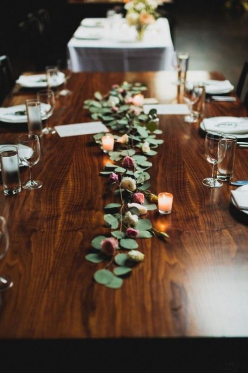 a delicate greeneyr and flower wedding table runner with some candles is a chic and stylish idea for a wedding