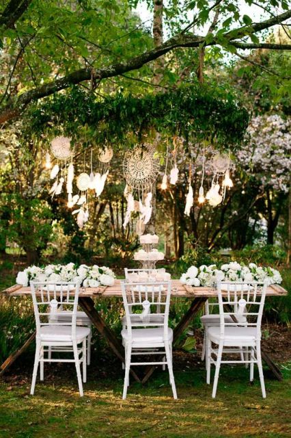 Dream catchers with feathers and bulbs hanging over the reception table is a cool way to add a boho touch to the space
