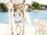 a boho beach dream catcher with crochet lace, long fringe, feathers and some white blooms for a boho beach wedding