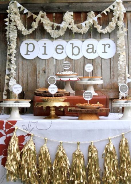a cozy rustic pie bar with paper garlands, a letter banner, mismatching stands including a rustic one with a wood slice and a garland with gold tassels is ideal for a fall wedding