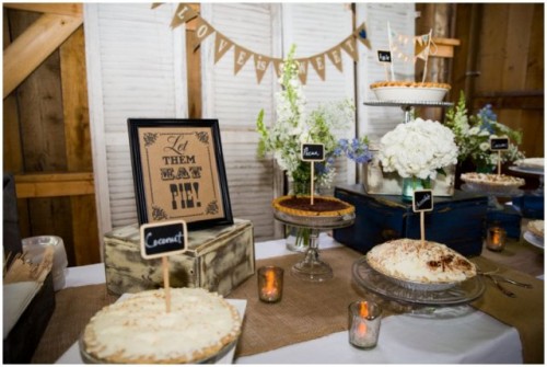 a rustic pie bar with a banner, some simple blooms, signs and tags, candles and pies on stands and plates