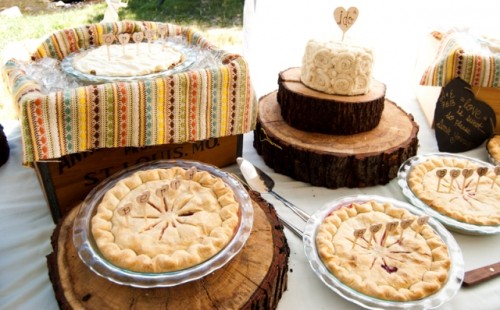 a rustic boho wedding with wood slices, a box with plates and a colorful towel and tasty pies and a wedding cake with a topper
