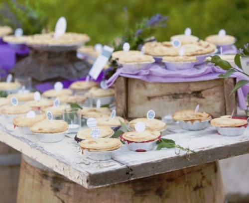 a lovely spring or summer wedding pie bar with crate and box stands, lilac linens, greenery and mini pies with toppers is a lovely and chic idea