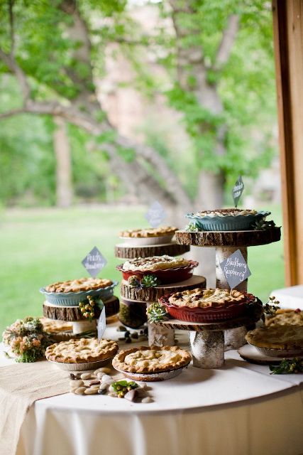 a rustic pie bar with wood slice stands, a burlap runner, some pebbles and greenery and blooms is ideal for any rustic or farmhouse wedding