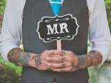 a stylish vintage-inspired groom’s look with a white shirt with cropped sleeves that show off the groom’s tattoos, a grey waistcoat, a turquoise tie