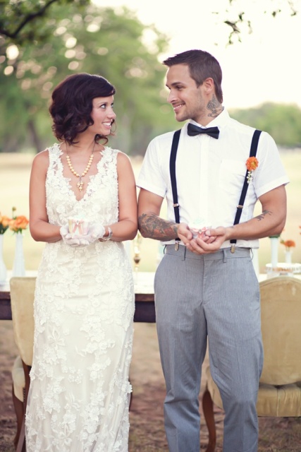 a vintage groom's look with a white short sleeved shirt, black suspenders and grey pants, a black bow tie is a lovely way to show off his arm tattoos