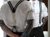 a stylish groom’s look with a white shirt, black pants, striped suspenders and a striped tie, bold tattoos on the arms