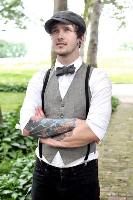 a vintage groom's look with a white shirt, a grey waistcoat, a black bow tie and suspenders, a cap and cuffed sleeves to show off the tattoos
