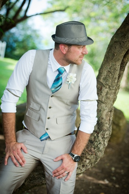 a neutral waistcoat and pants, a white shirt, a turquoise tie and a grey hat