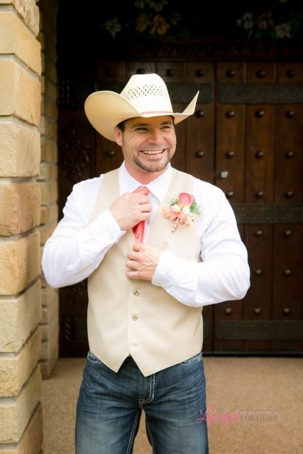 a cowboy-inspired groom's look with jeans, a white shirt, a neutral waistcoat, a coral tie and a cowboy hat