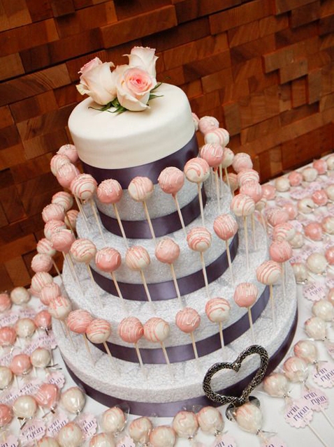 a small one-tier wedding cake on a stand with pink roses and pink cake pops served around the cake as an alternative to a bigger wedding cake