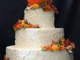 a white patterned buttercream wedding cake with bright blooms, leaves and a faux pumpkin on top is refined