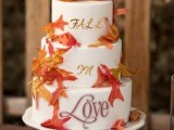 a white buttercream wedding cake with letters, bright leaves and sugar pumpkins is a very cool and cozy idea for a fall wedding