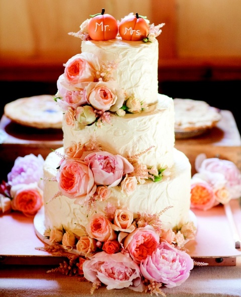 a white textural buttercream wedding cake decorated wiht pink peonies and roses and topped with two sugar pumpkins is ideal for a fall wedding