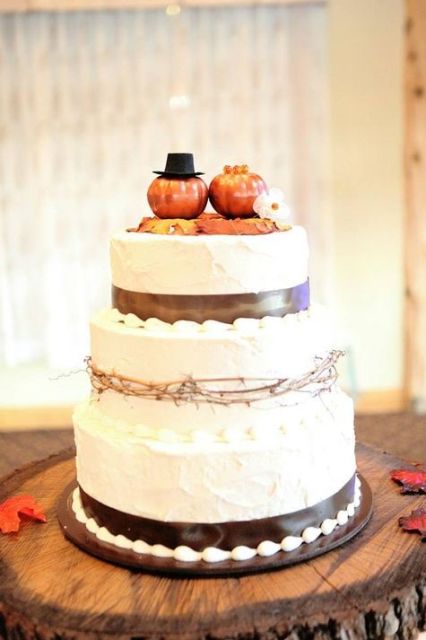a white buttercream wedding cake with brown ribbons, twigs and pumpkins on top is a very lovely and cool idea