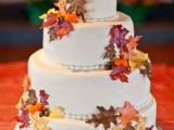 a white buttercream wedding cake with colorful faux leaves and a gold pumpkin topper is a lovely and fun idea