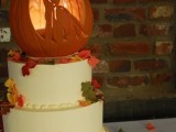 a white buttercream wedding cake with a carved pumpkin and a candle on top plus some colorful leaves is a gorgeous idea to rock for the fall or Halloween