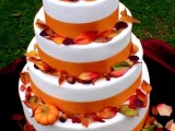 a white buttercream wedding cake with orange ribbons, colorful fall leaves and mini pumpkins is a fantastic idea