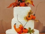 a white buttercream wedding cake with patterns, faux pumpkins, gourds, twigs and leaves is a gorgeous idea for a rustic fall wedding