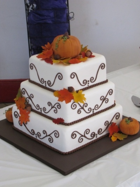 a square white wedding cake with patterns, with bright fall leaves and a pumpkin on top is a cool idea for a rustic fall wedding