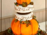 a creative wedding cake with white patterned tiers, orange pumpkins, faux leaves and twigs on top is a lovely idea