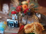 a vintage cluster wedding centerpiece of a stack of books, a vintage camera and bright blooms is amazing for a bold wedding