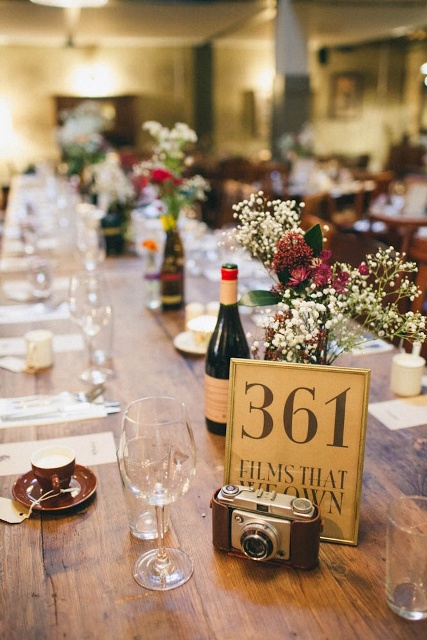 a simple and lovely cluster wedding centerpiece of burgundy blooms and baby's breath, a camera, a table number is a pretty idea for a vintage wedding