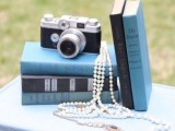 a refined vintage wedding centerpiece of a stack of books, a vintage camera and pearl strands is an awesome idea