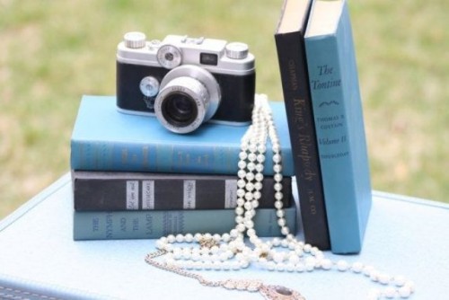 a refined vintage wedding centerpiece of a stack of books, a vintage camera and pearl strands is an awesome idea