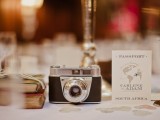 a vintage camera wedding centerpiece of a stack of books, a vintage camera and a table name is a great idea