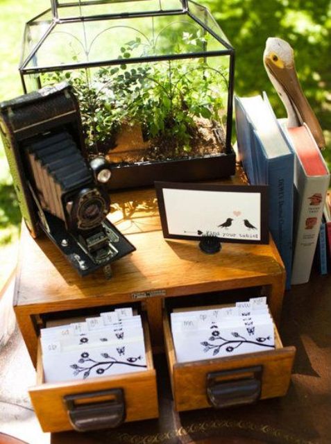 a vintage wedding decoration of a wooden box with cards, a vintage camera and soem greenery in a terrarium is amazing and very chic