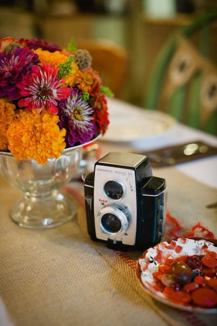 a jewel-tone wedding centerpiece of bold blooms, a metallic bowl and a vintage camera is a lovely idea for a fall wedding