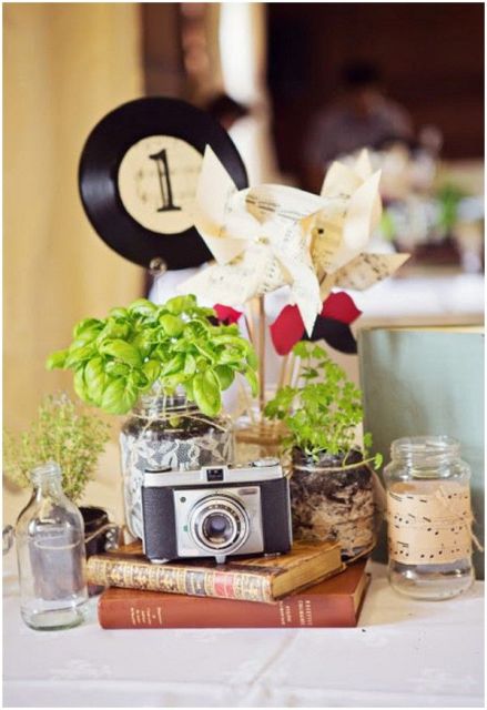 a cluster vintage wedding centerpiece with a stack of vintage books, potted greenery, a vintage camera and a paper fan is cool and lovely