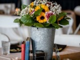 a vintage rustic wedding centerpiece of a bucket with sunflowers and baby’s breath, a stack of vintage books and a vintage camera plus candles around
