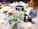 a vintage cluster wedding centerpiece of a stack of books, vintage cameras and pale greenery and white blooms