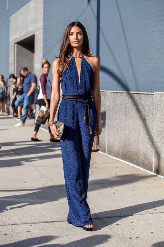 a navy print jumpsuit with a deep neckline, no sleeves and wideleg pants, a black rope sash and acool shiny clutch