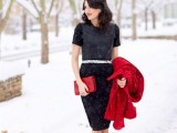 a classic black sheath knee dress with a high neckline, short sleeves, a shiny sash, silver shoes, a red clutch and a red coat