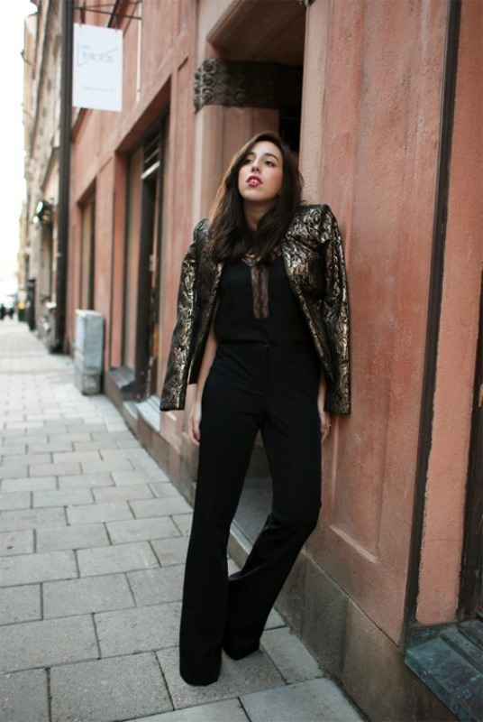 A black jumpsuit with a covered plunging neckline, a gold and black shiny cropped jacket