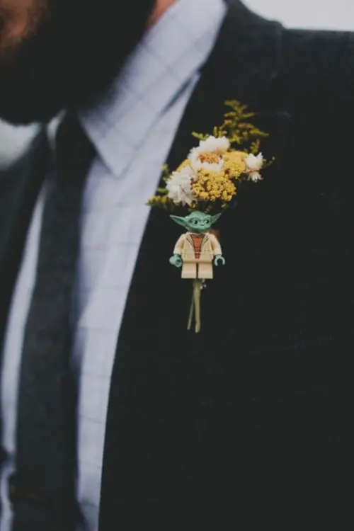 a small and fun Star Wars wedding boutonniere with white and yellow blooms and a little Yoda figurine is a fun idea to accessorize a groom's look