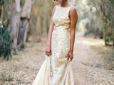 a neutral sleeveless A-line wedding dress with a high neckline and shiny gold leaf appliques and a belt is very chic and bold