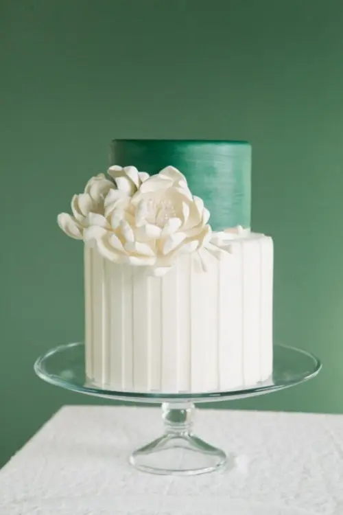 a bold round green and white wedding cake with a striped and sleek tier and some white sugar blooms for an elegant wedding