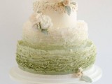 a white and ombre green wedding cake with ruffles, white and blush blooms and pale leaves is refined and chic