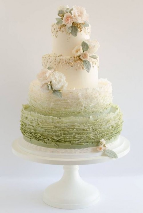 a white and ombre green wedding cake with ruffles, white and blush blooms and pale leaves is refined and chic
